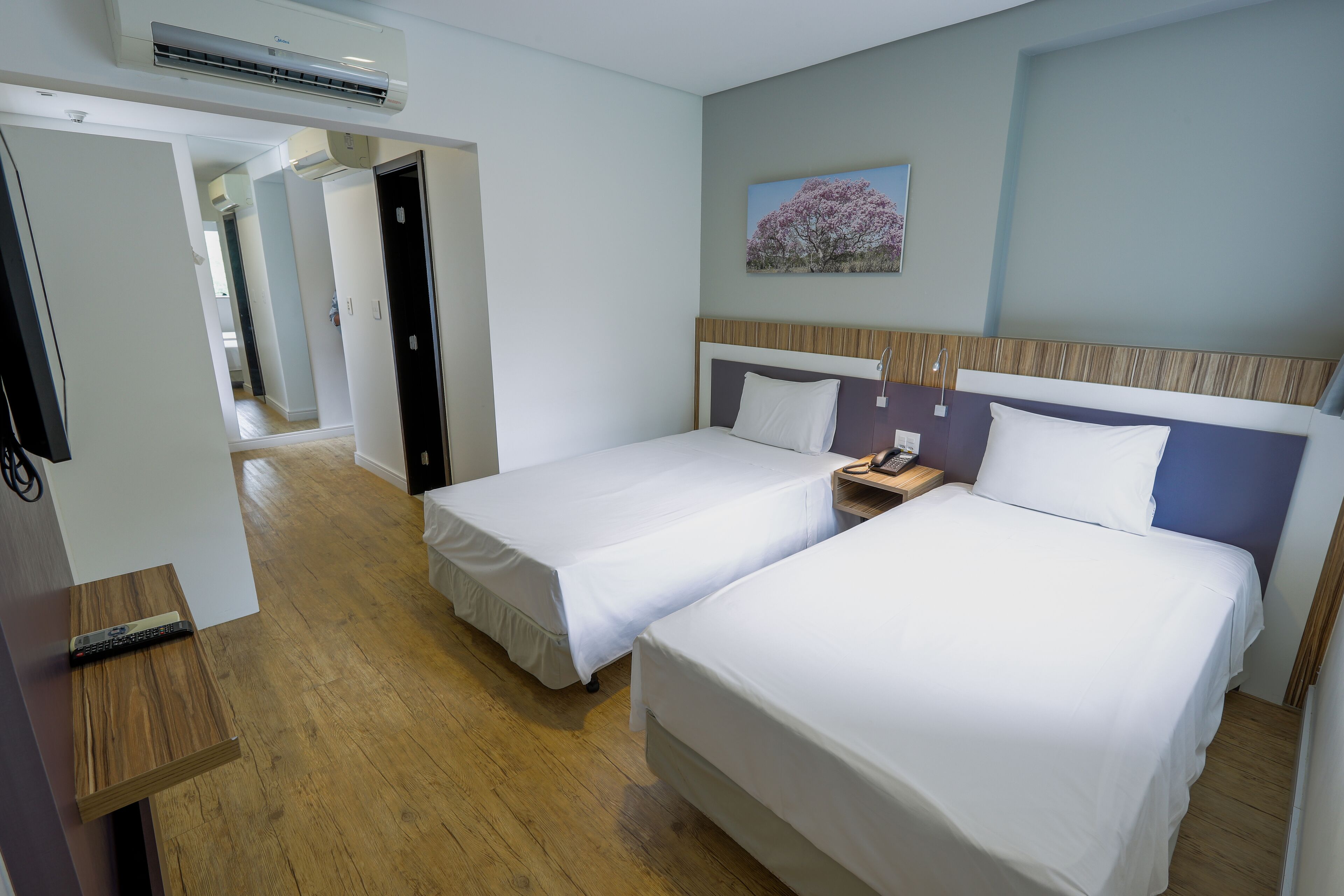 A hotel room with two beds, a wooden floor, a painting on the wall, and a phone on the nightstand.