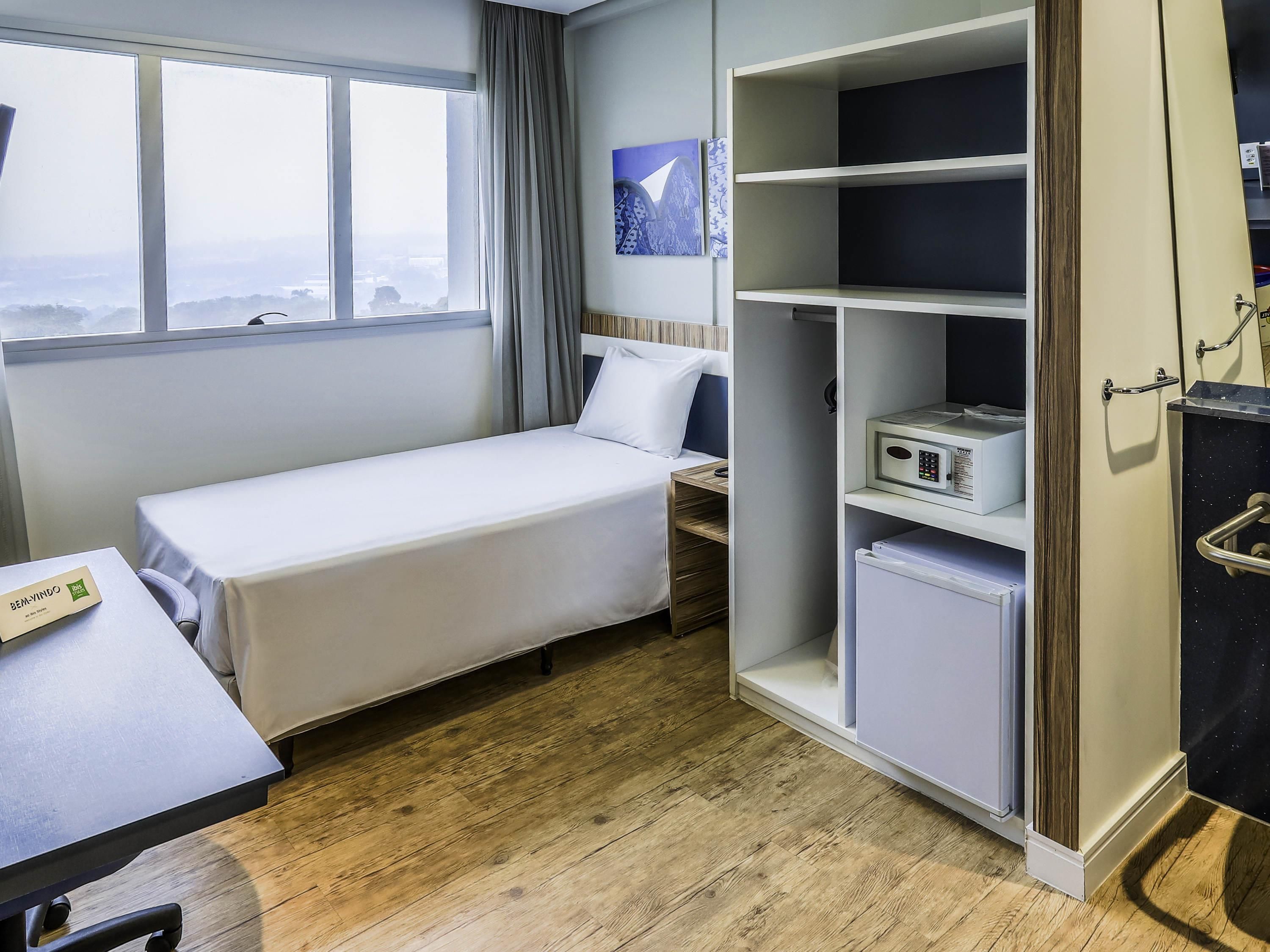 A hotel room with a single bed, a desk, a wardrobe, and a view through a window.