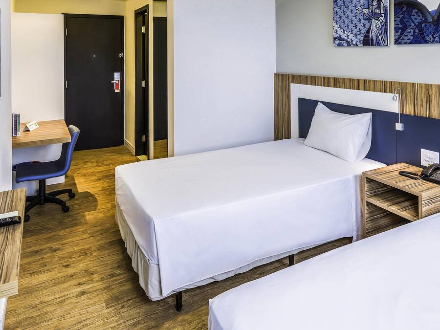 Habitación de hotel con dos camas individuales, un escritorio con silla, teléfono y una obra de arte en la pared.