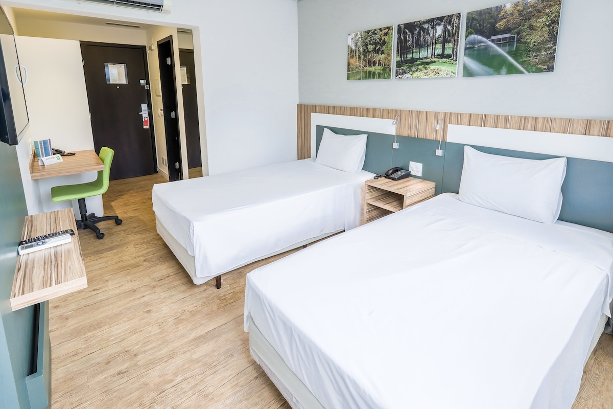 Habitación de hotel con dos camas individuales, un escritorio con silla, una mesita y un teléfono en la pared.