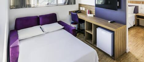 Une chambre d’hôtel équipée d’un lit, d’un bureau, d’une chaise, d’une télévision et d’un petit réfrigérateur.