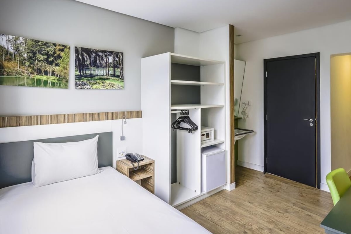Habitación de hotel con cama, armario, escritorio y teléfono, y una puerta.
