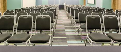 A conference room with rows of chairs, a projector screen, and a podium at the front.