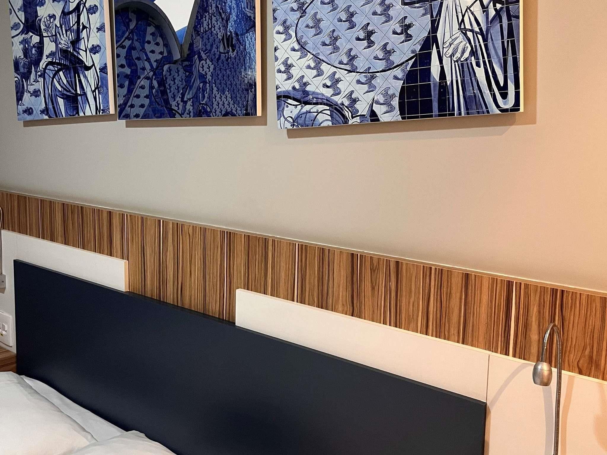 Un dormitorio con cabecera de madera, una cama y tres obras de arte colgadas en la pared.