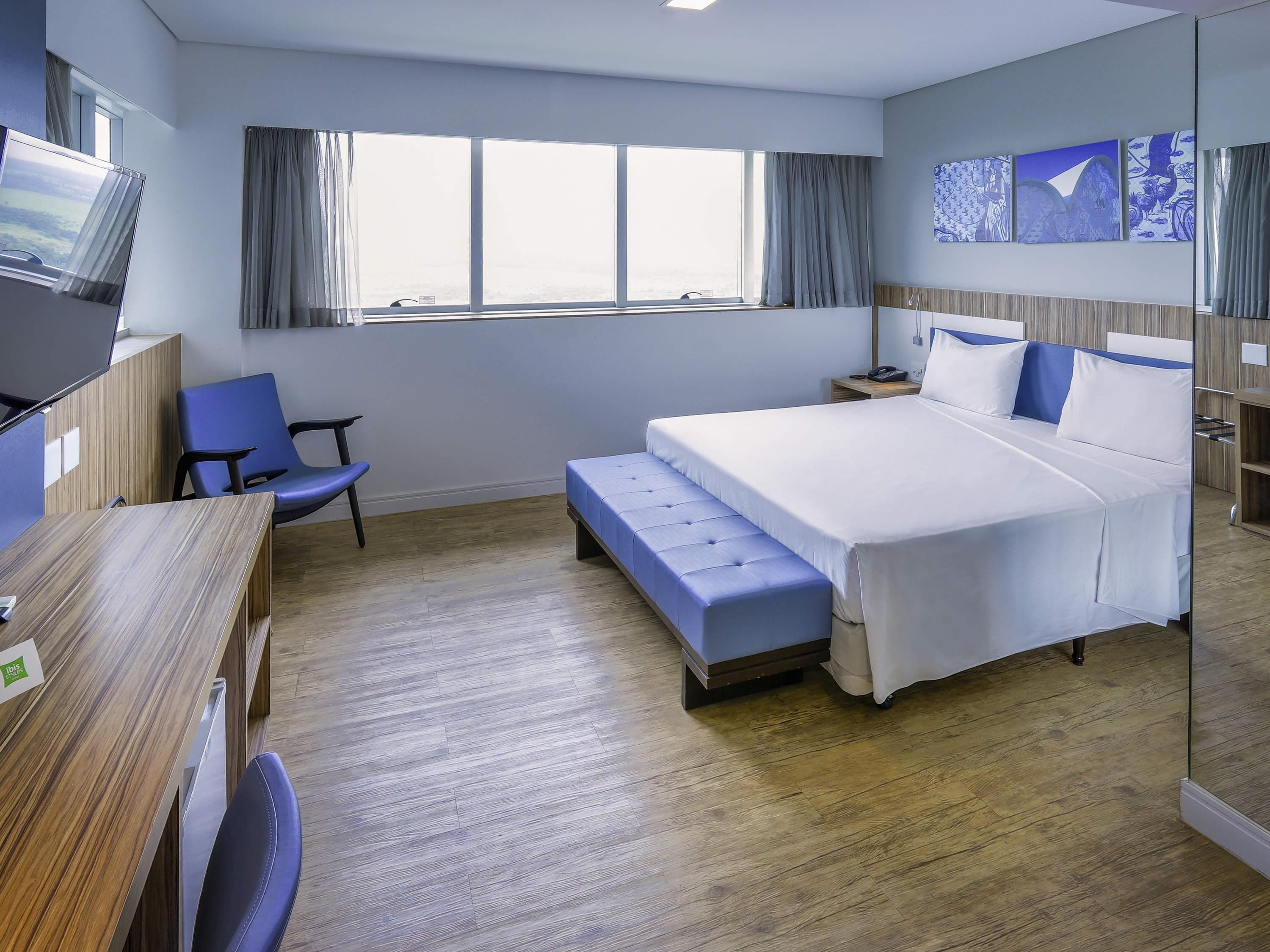 A hotel room with a bed, a desk, a chair, a television, and a window with curtains.