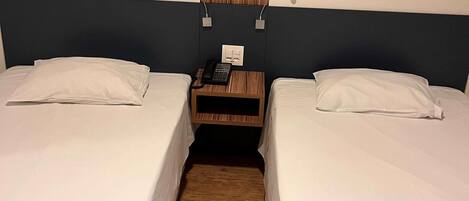 Habitación de hotel con dos camas individuales, una mesita de noche de madera con teléfono y una lámpara fijada a la pared.