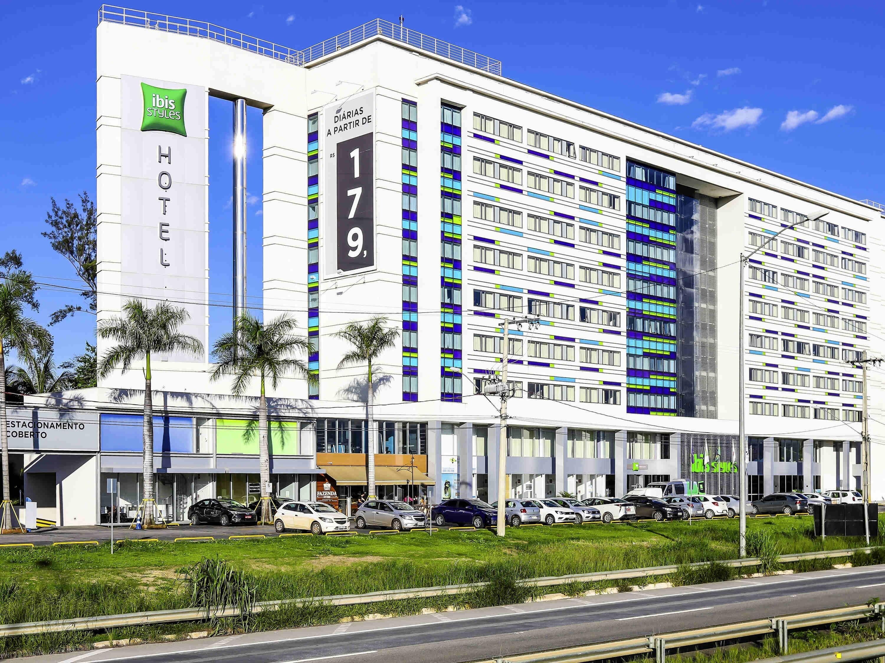 A modern hotel with a prominent 'HOTEL' sign, multiple floors, and a parking lot with several cars.