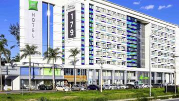 A modern hotel with a prominent 'HOTEL' sign, multiple floors, and a parking lot with several cars.