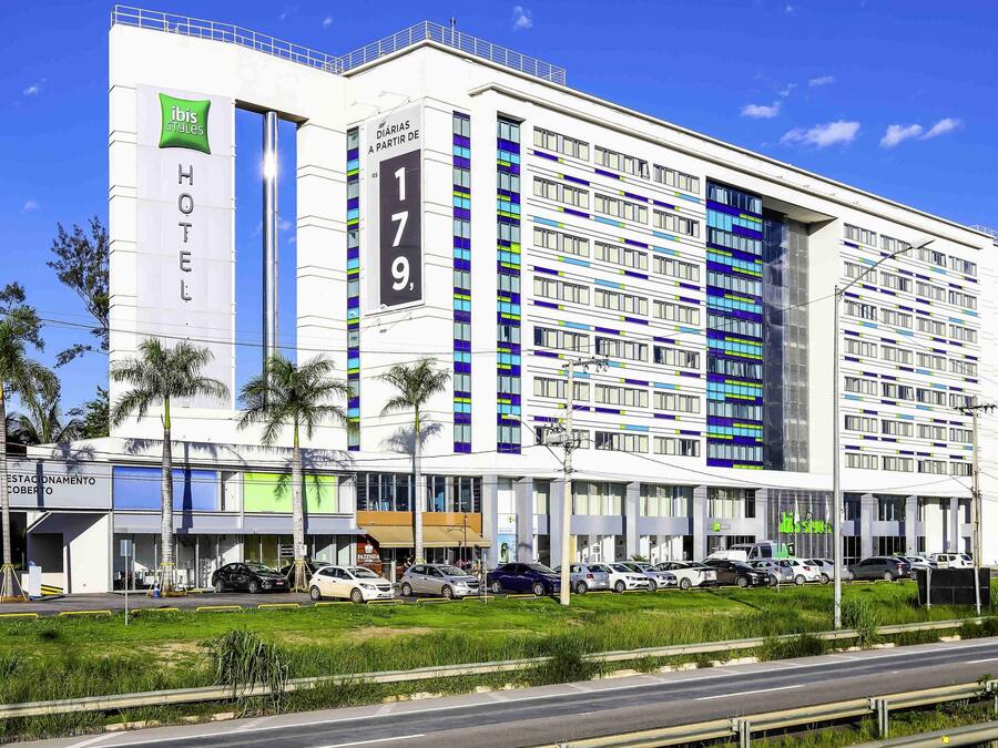 A modern hotel with a prominent 'HOTEL' sign, multiple floors, and a parking lot with several cars.