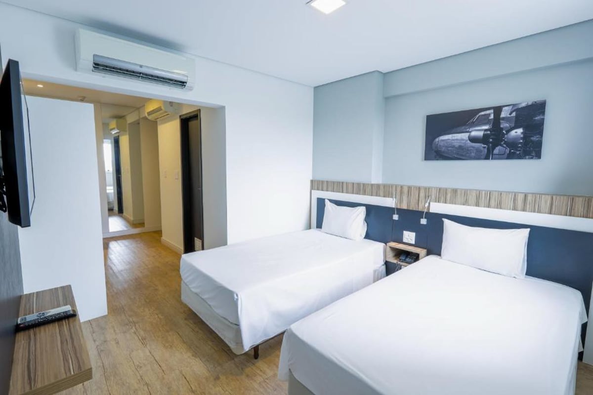 Una habitación de hotel con dos camas, televisión y aire acondicionado.