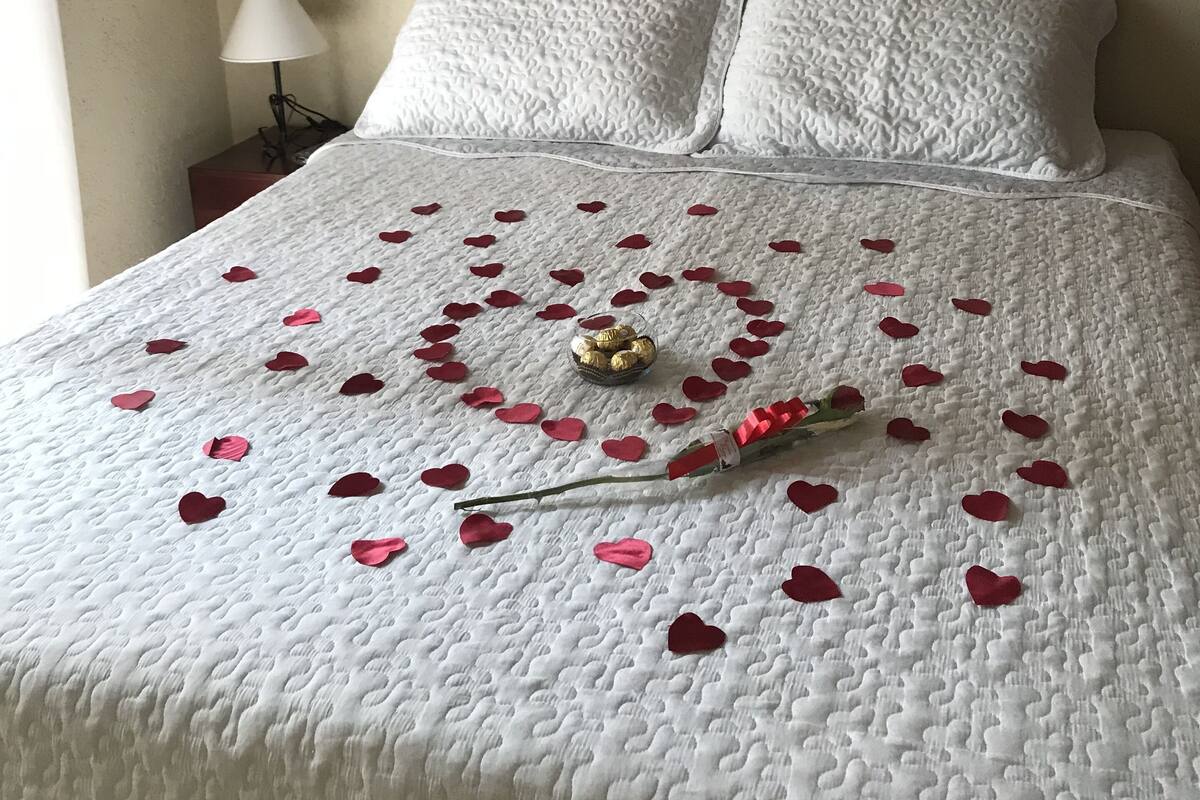 A bed with a white quilt, red heart-shaped decorations, and a bouquet of flowers.