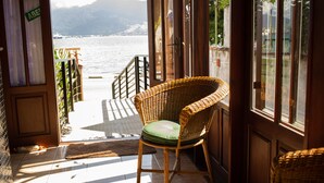 A wicker chair with a green cushion in a room with a view of a body of water and mountains. - Pousada Irmaos do Mar (Ilhabela)