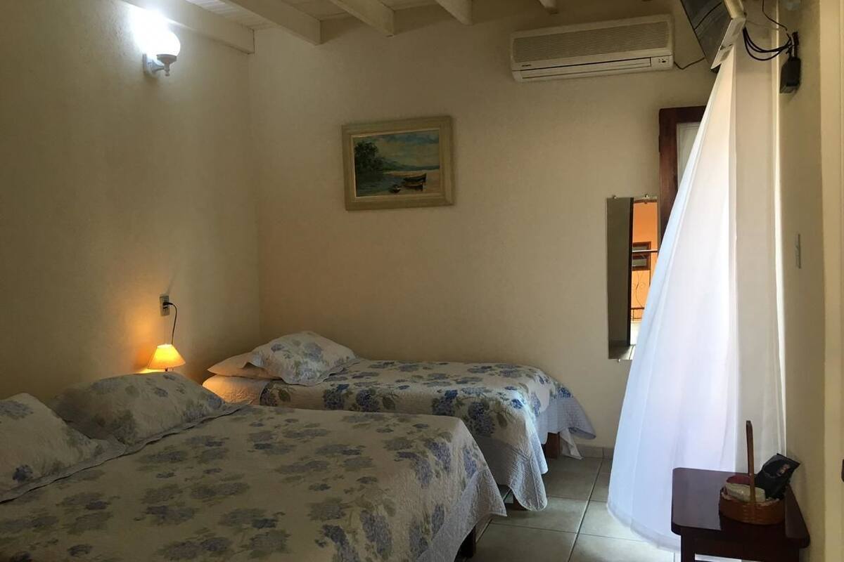A room with two beds, a painting on the wall, a ceiling fan, and a window with curtains.