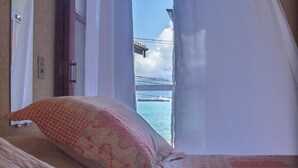 A bedroom with a bed, pillows, and a view of a body of water through a window. - Pousada Irmaos do Mar (Ilhabela)