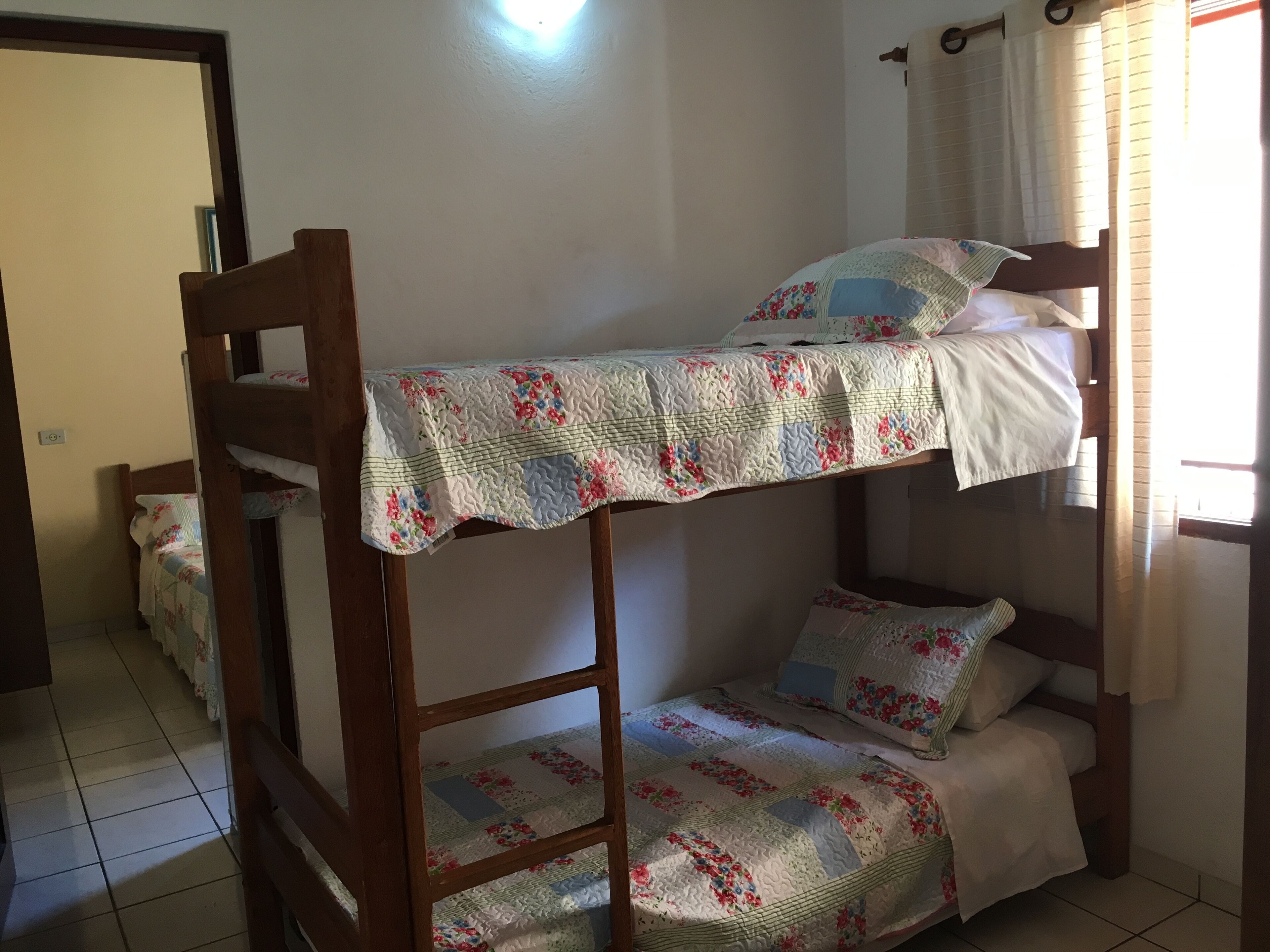 Una cama individual con ropa de cama floral en una habitación con suelo de baldosas y una puerta al fondo.