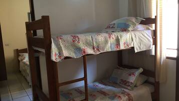Una cama individual con ropa de cama floral en una habitación con suelo de baldosas y una puerta al fondo.