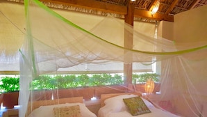 Una habitación con una cama bajo una mosquitera, vigas de madera en el techo y vistas al verde exterior.