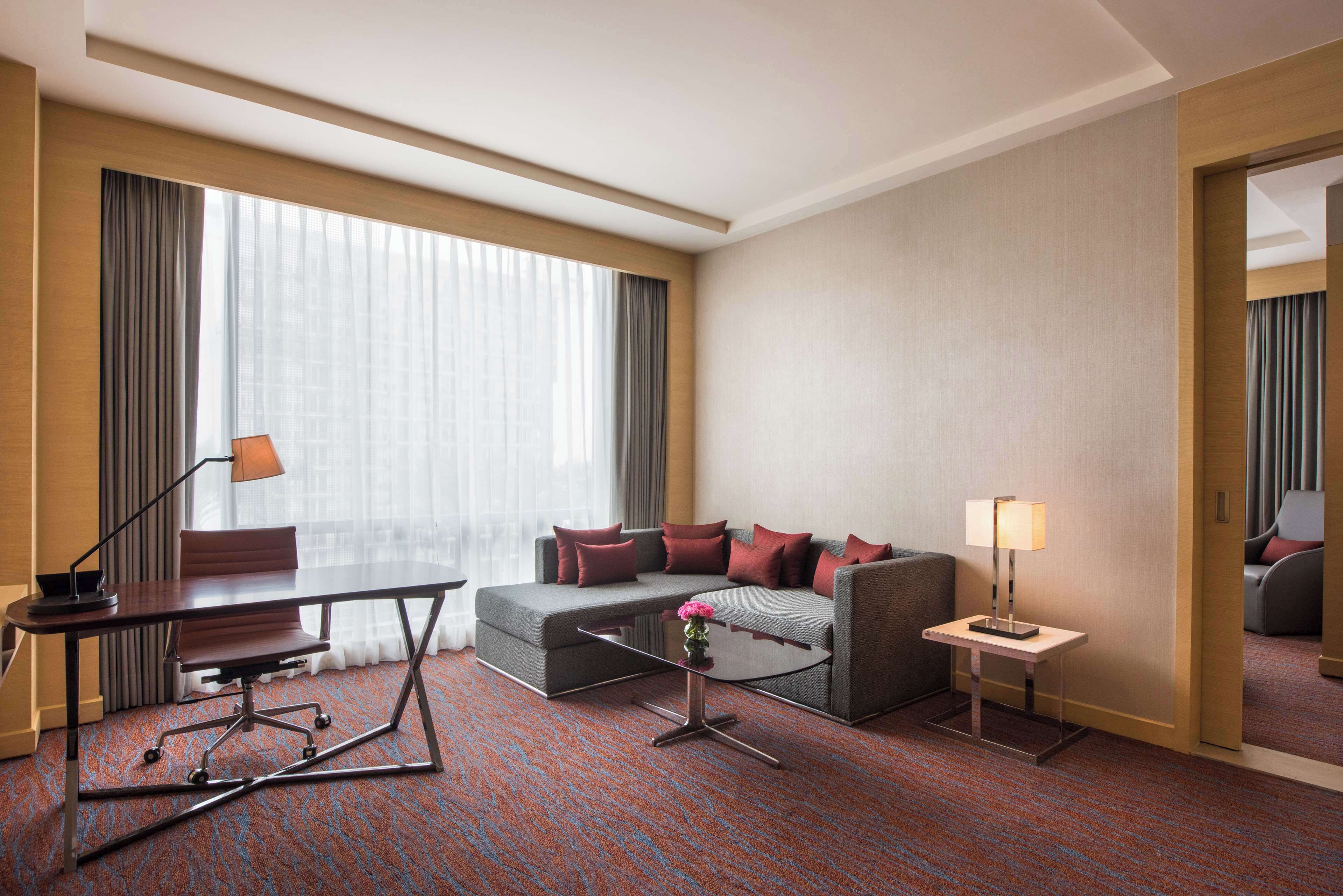 A hotel room with a sofa, a desk, a coffee table, and a lamp.