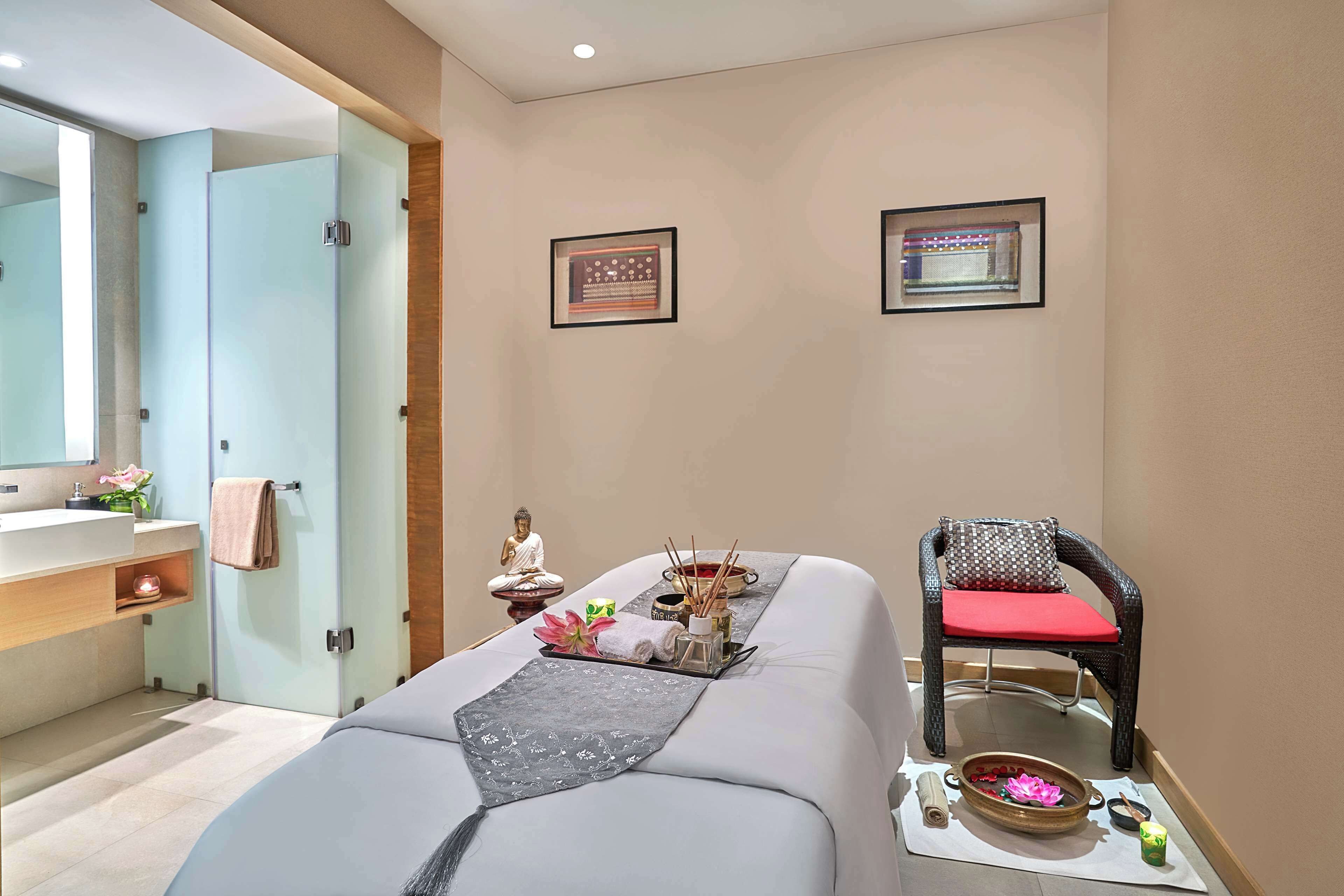 A spa room with a massage table, a chair, a small Buddha statue, and a wall-mounted picture.