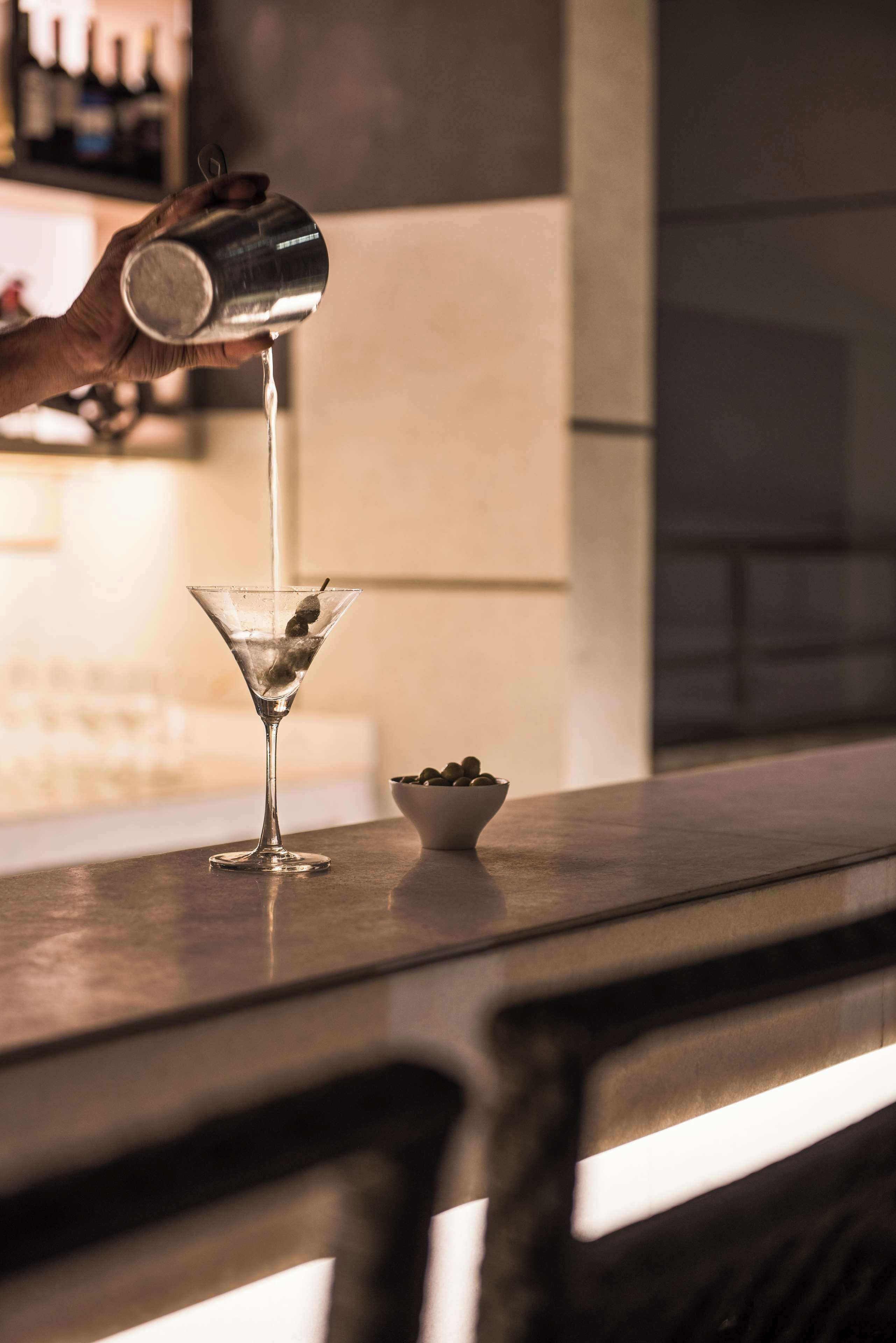 A hand pouring a drink into a martini glass on a bar counter.