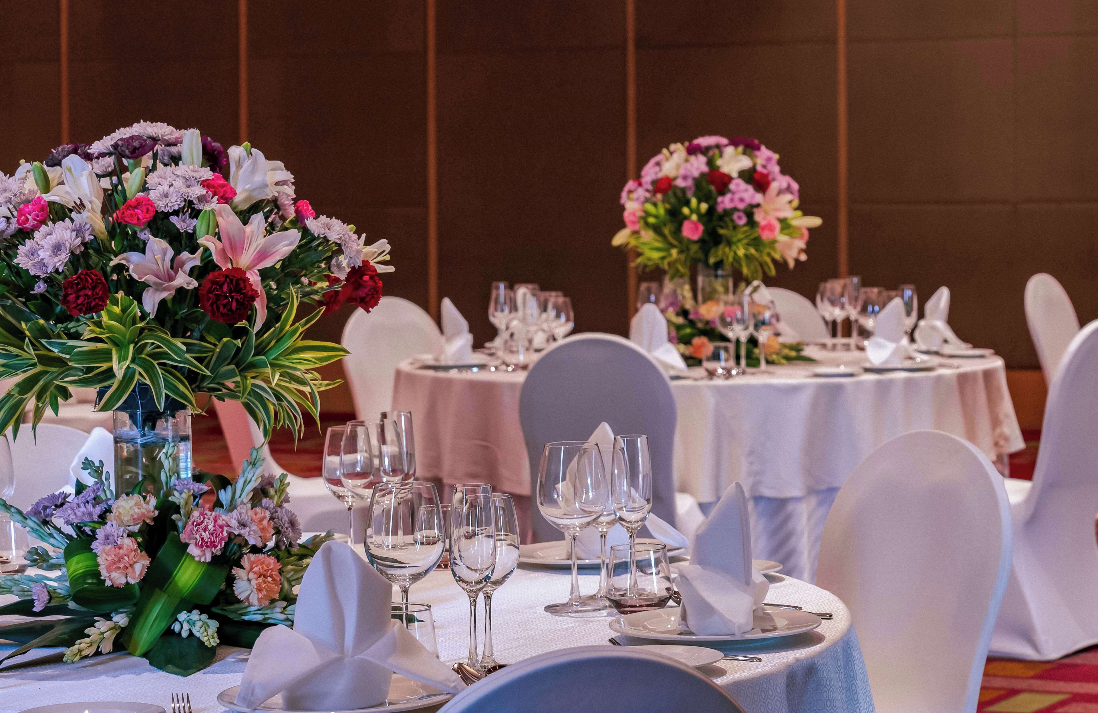 Salão de banquetes com mesas redondas dispostas para refeições, cada uma com toalhas brancas e copos.