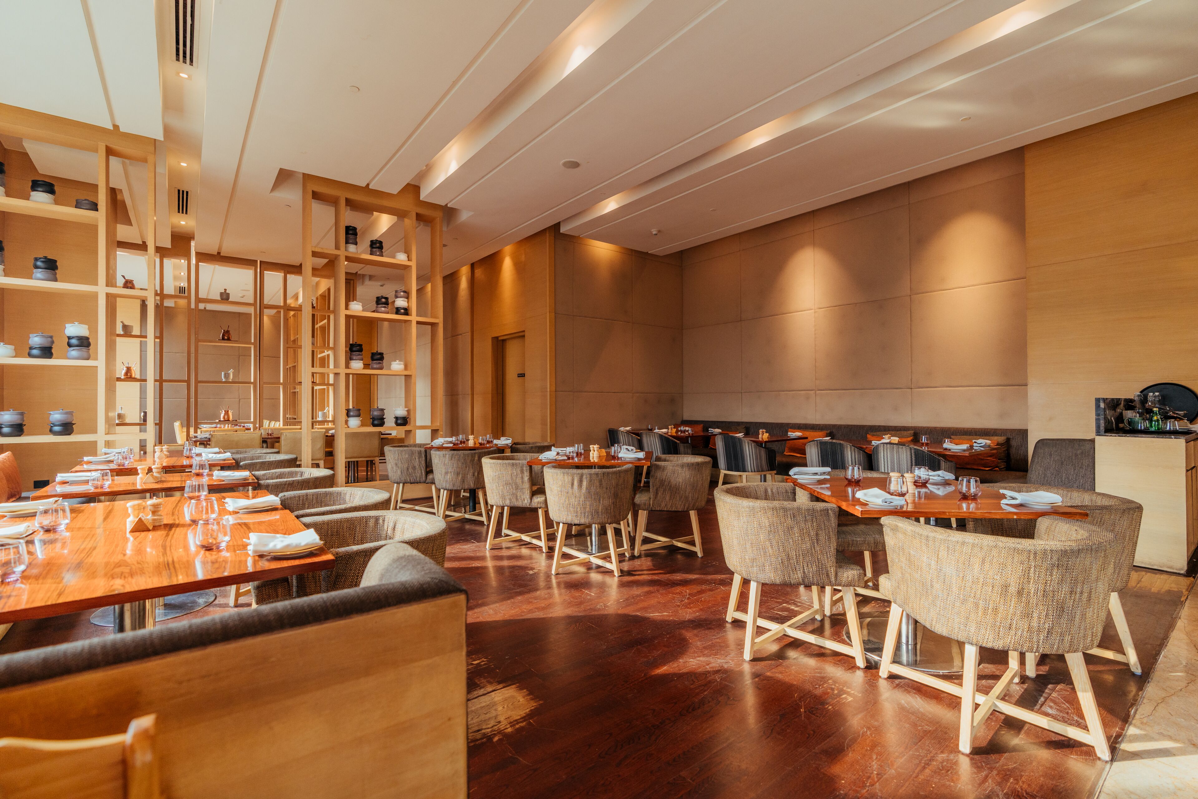 A modern dining area with wooden tables and chairs, a large wooden bookshelf, and a polished floor.