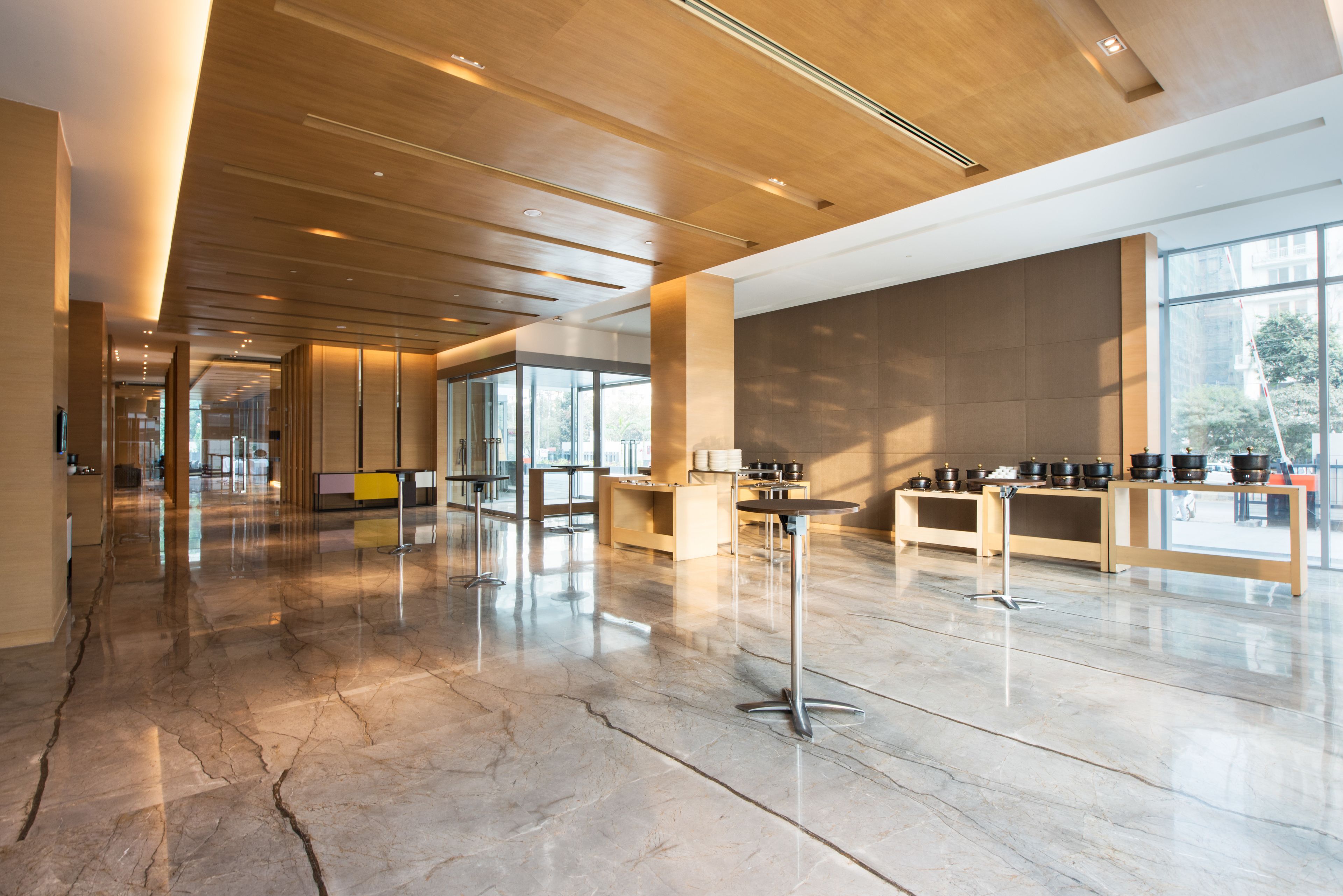 A spacious lobby with a polished marble floor, wooden ceiling, and large windows offering natural light.