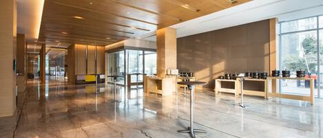 A spacious lobby with a polished marble floor, wooden ceiling, and large windows offering natural light.