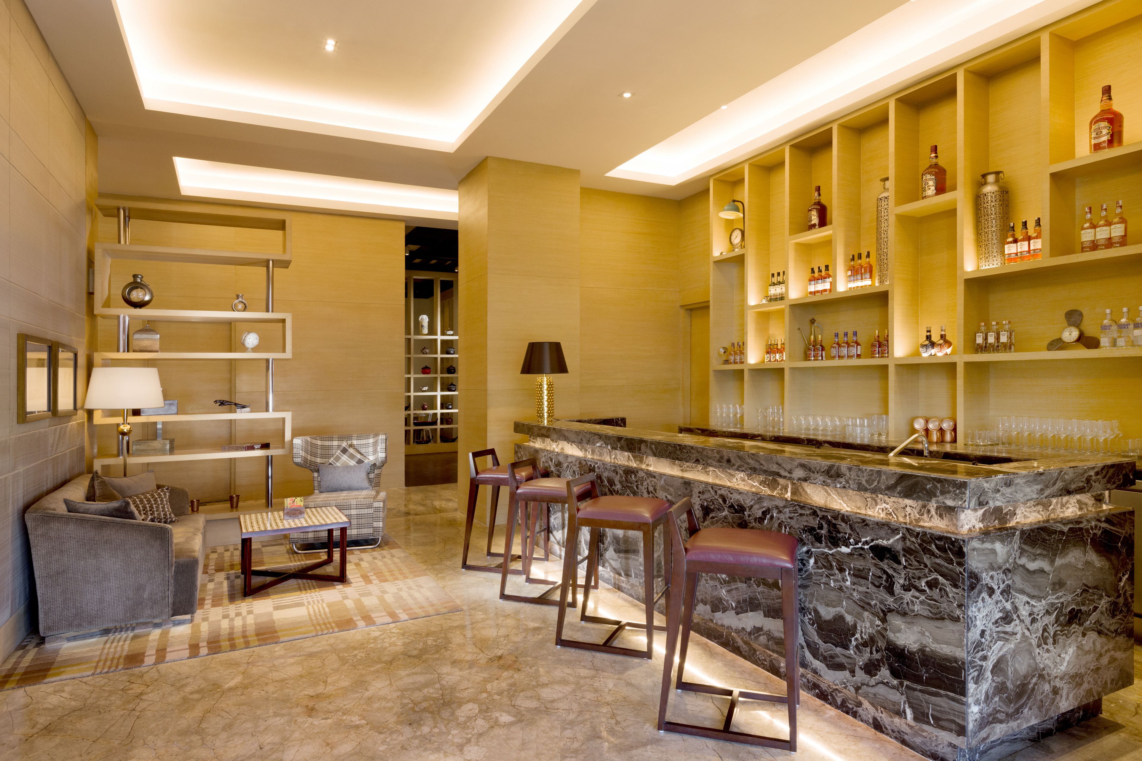 A modern bar area with marble countertops, bar stools, and shelves stocked with bottles.