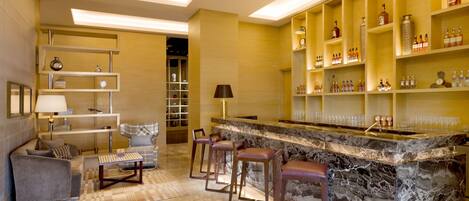 A modern bar area with marble countertops, bar stools, and shelves stocked with bottles.