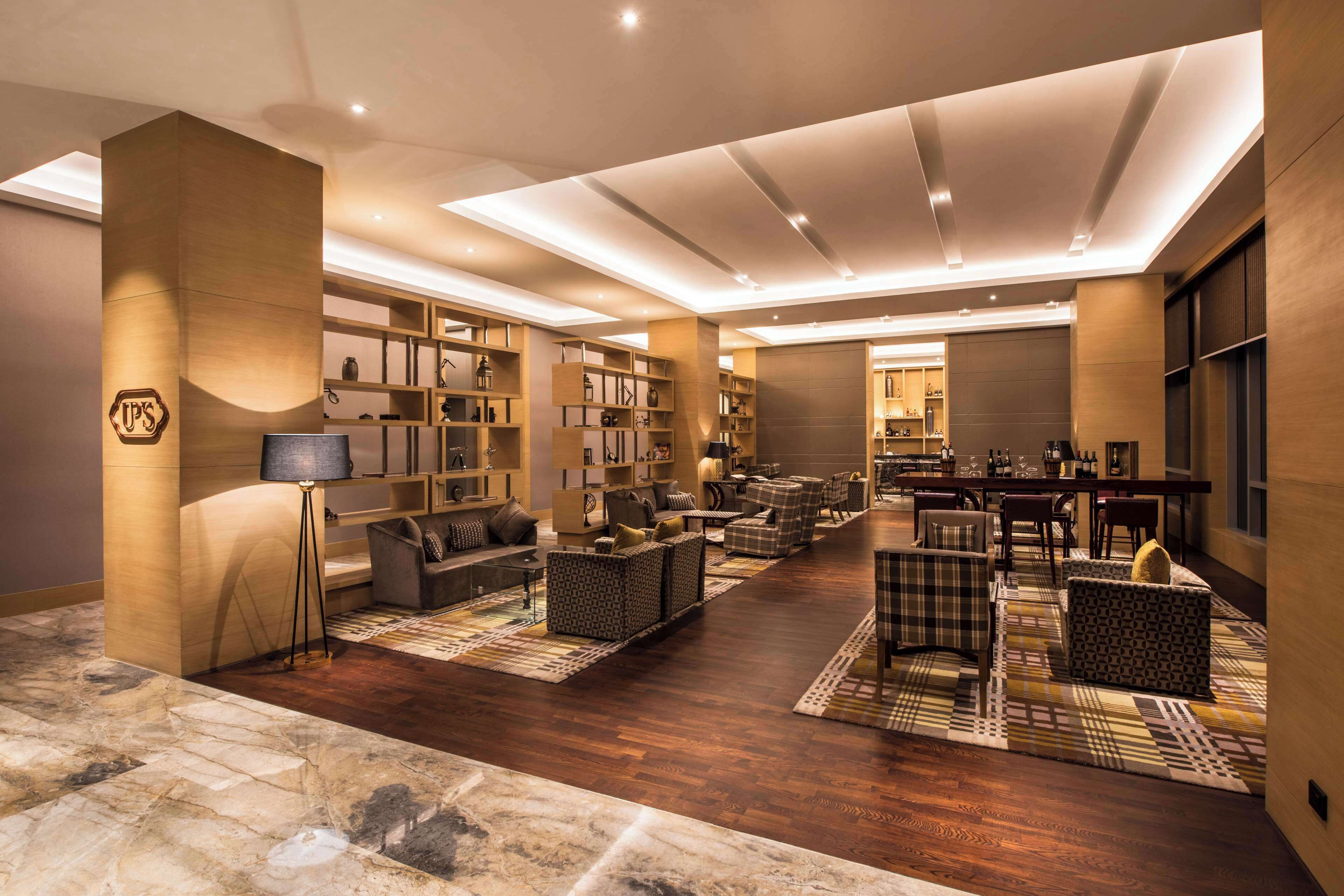 A spacious hotel lobby with a central seating area, a large bookshelf, and a dining area.