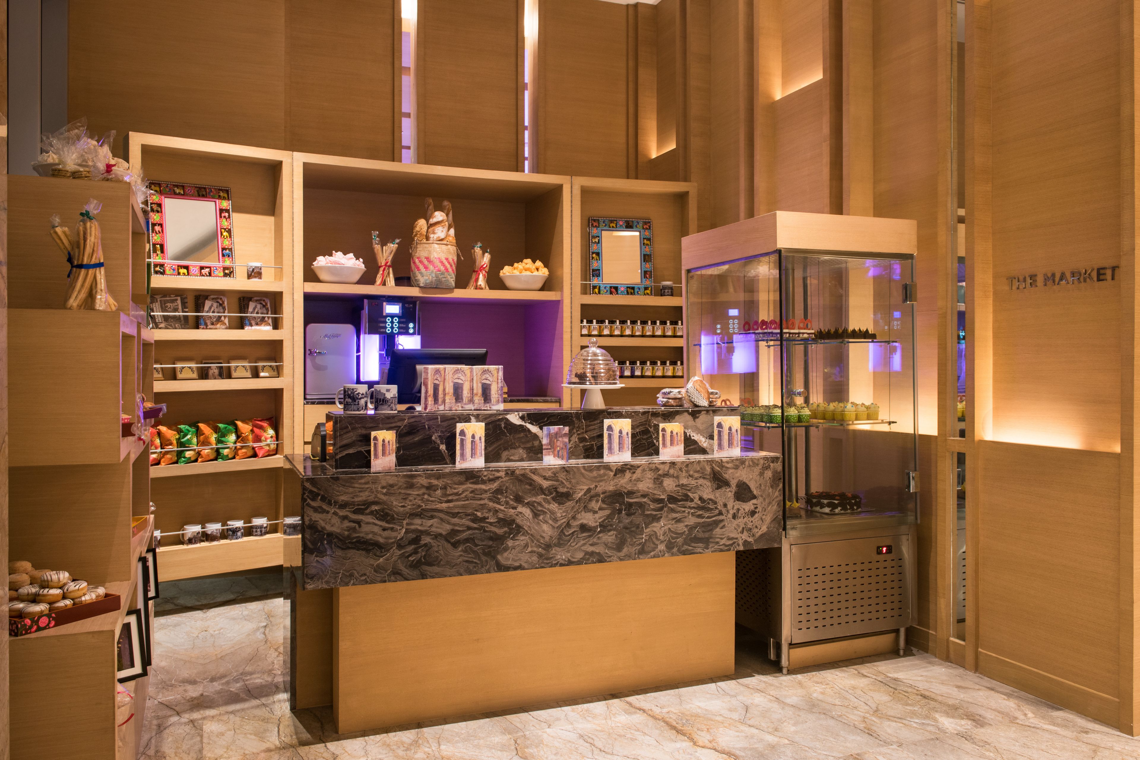 Ein Hotel-Rezeptionsbereich mit Marmorarbeitsplatten, Holzregalen und einer Kühlvitrine.