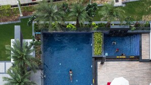 An aerial view of a rooftop swimming pool with a 'No Diving' sign, surrounded by palm trees, red and white sun loungers, and a brick wall. - Hyatt Regency Lucknow (Lucknow)