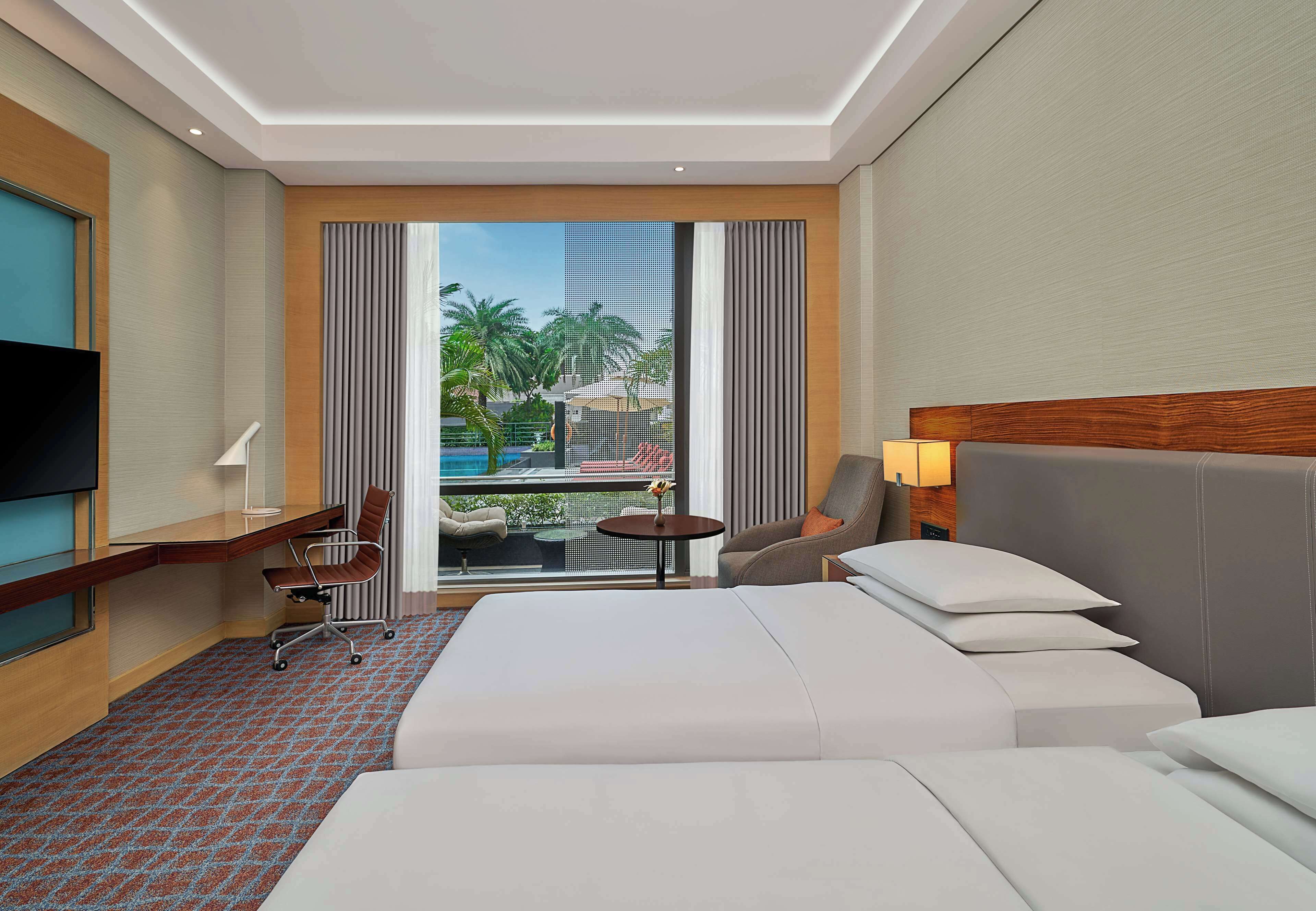 A hotel room with a large bed, a desk, a chair, a small table, and a TV.