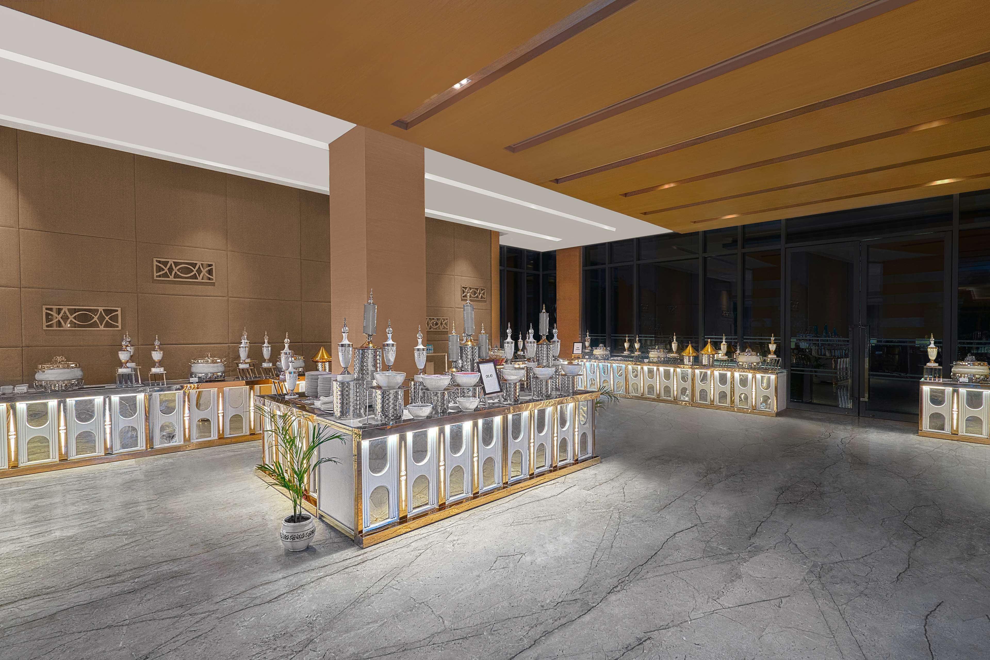Un vestíbulo espacioso con piso de mármol, una recepción central decorada con trofeos y un amplio ventanal con vistas a la ciudad.