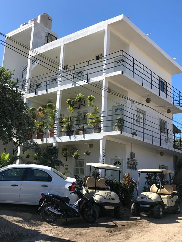 A multi-story building with balconies, potted plants, and a white car parked in front. - Sayulita Kart Inn (Sayulita)