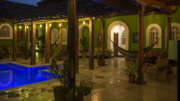 Un área de piscina con una hamaca, pilares de madera y plantas en macetas.