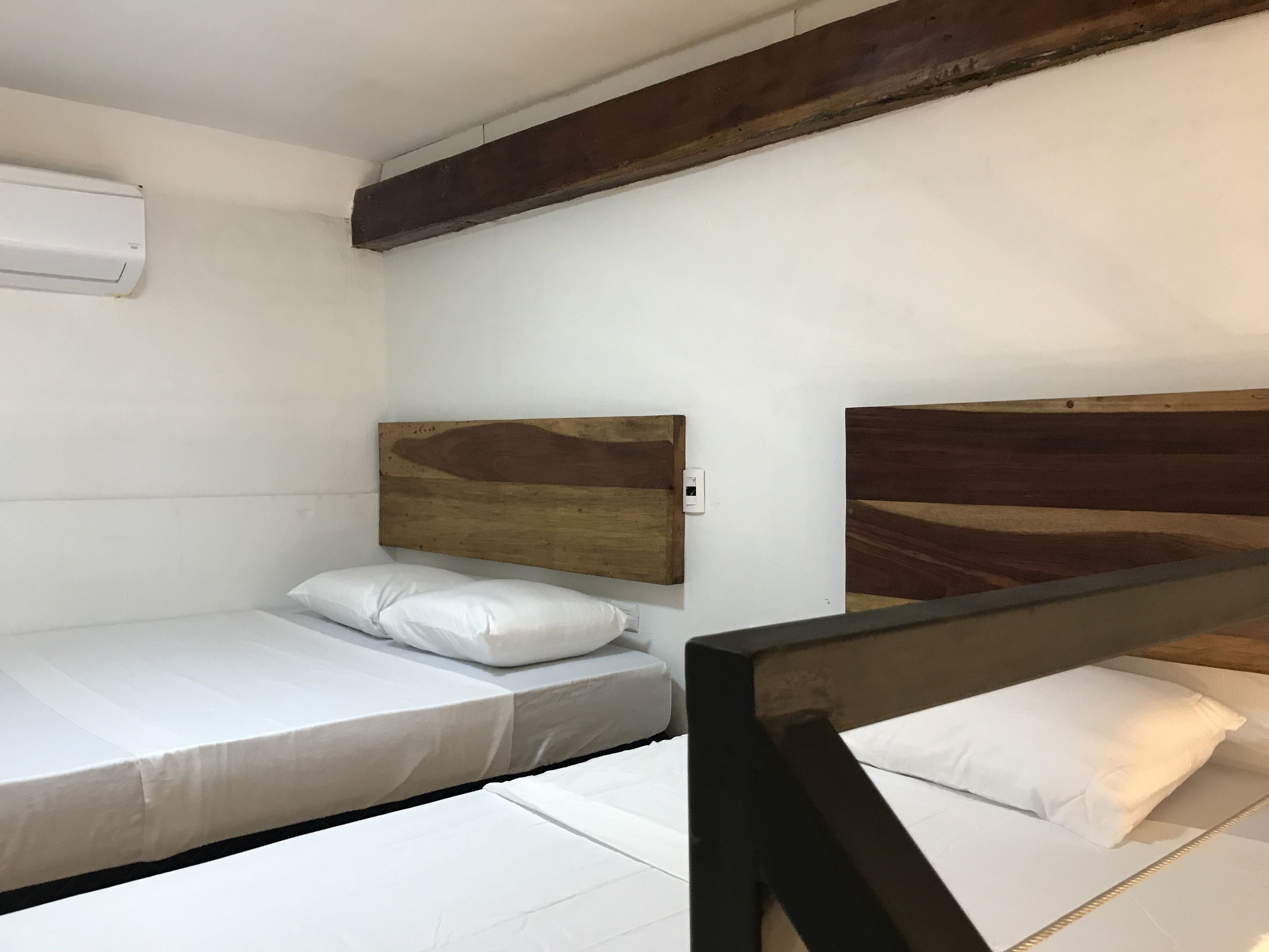 A small, single-bed room with a wooden headboard, white bedding, and a white wall.