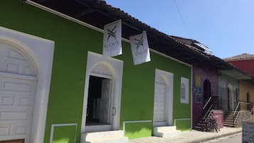 A green building with white doors and windows, a sign for El Caite City Hostel, and a staircase leading to a door.