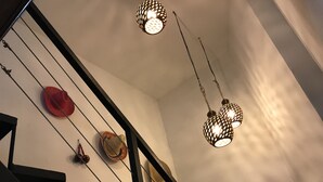 Una escalera con barandilla negra, un sombrero rojo y dos lámparas esféricas con un diseño ornamental.