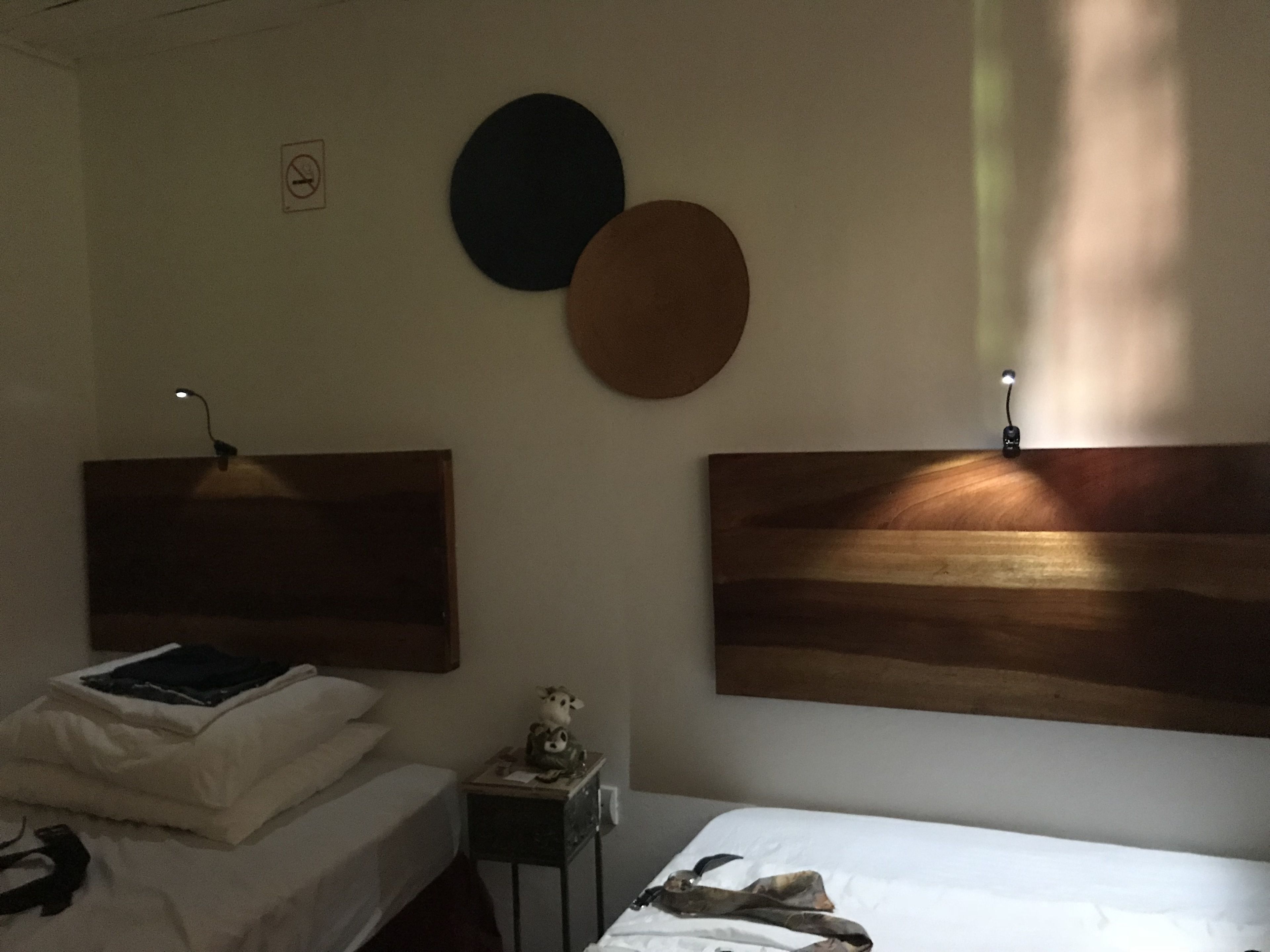 Habitación de hotel con dos camas, una mesita de noche y espejos redondos montados en la pared.