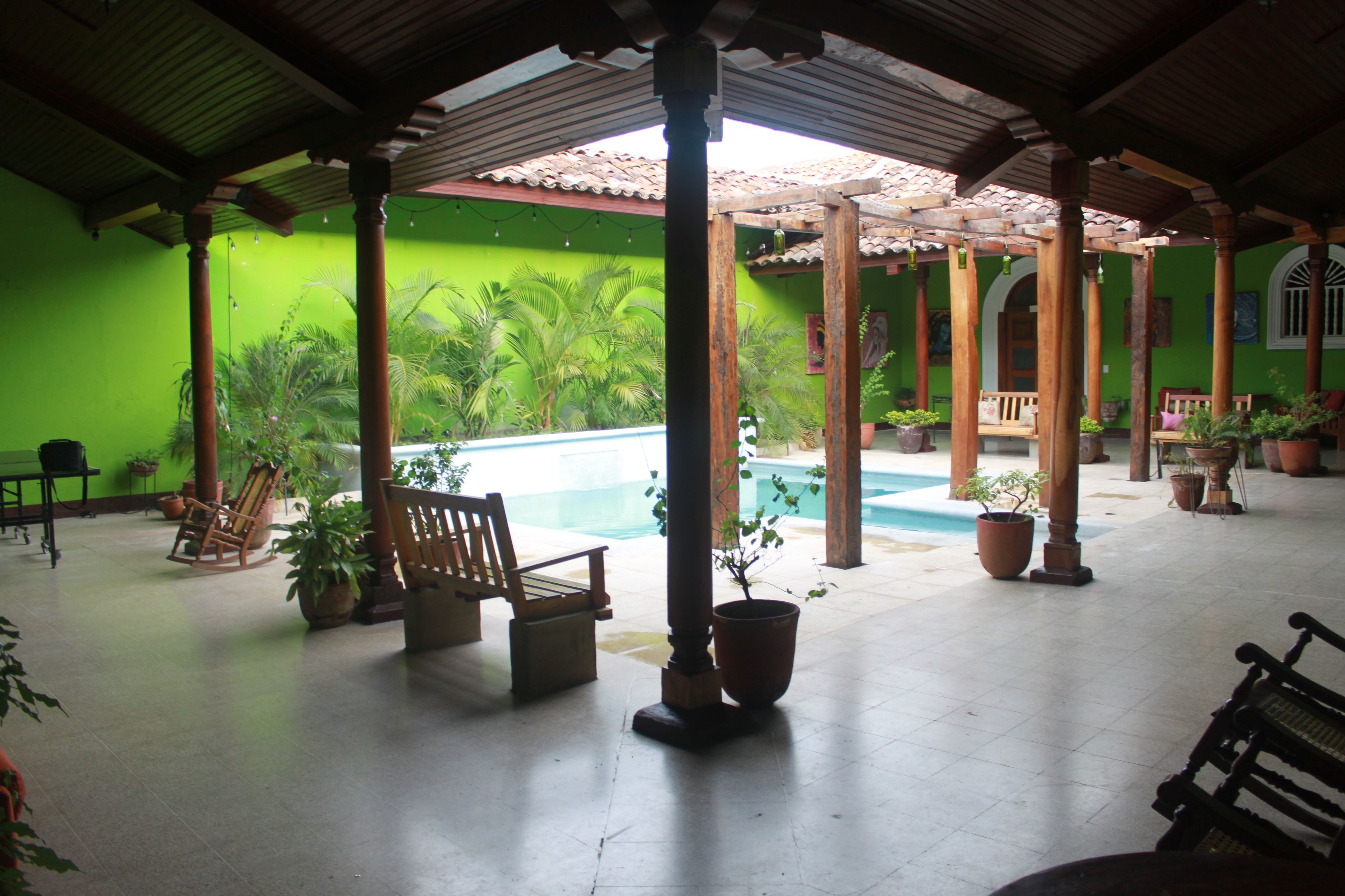 A covered outdoor area with a pool, wooden furniture, and potted plants.