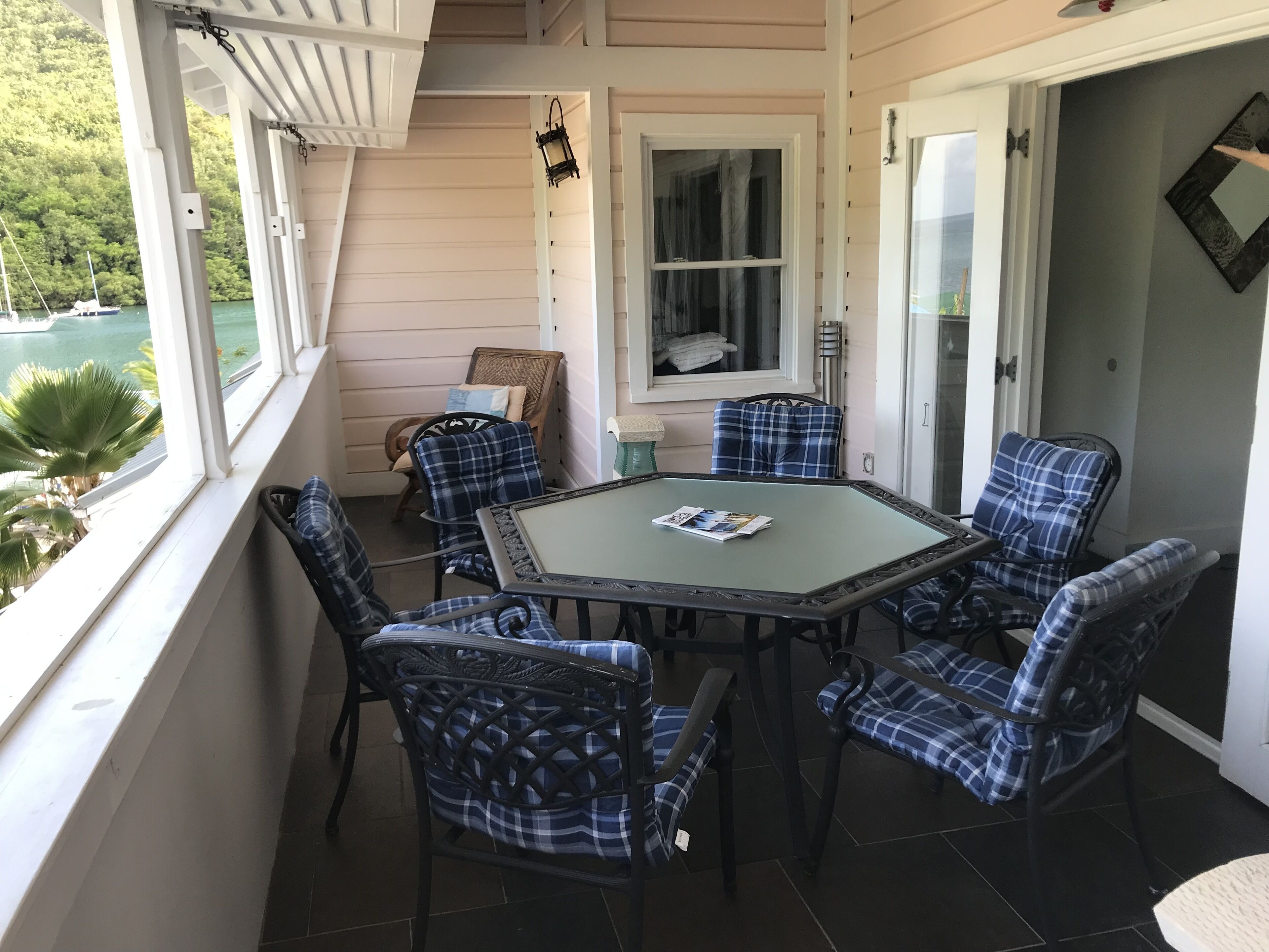 A covered patio with a glass table surrounded by plaid chairs, overlooking a body of water.