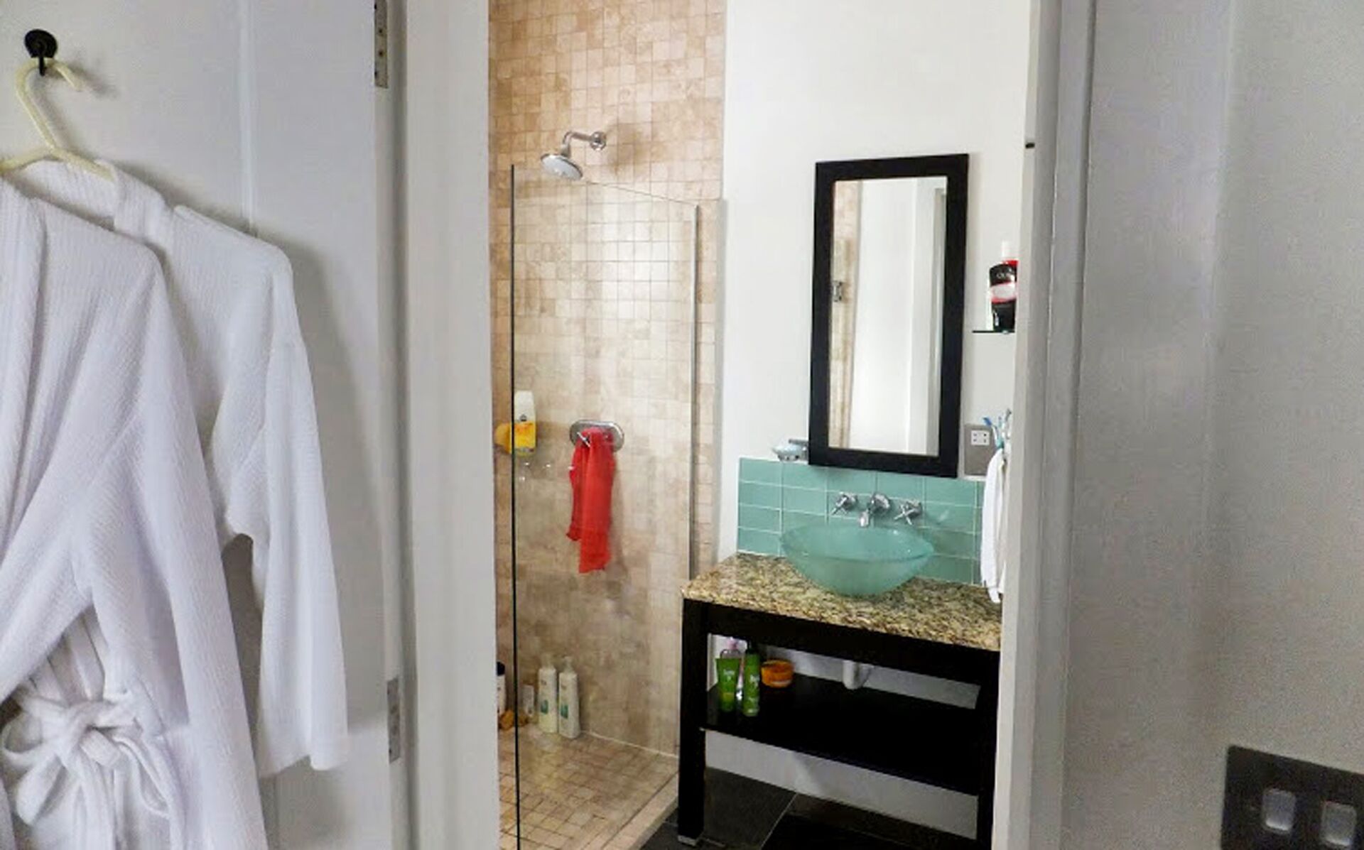 A bathroom with a glass shower enclosure, a white towel rack, a sink with a green countertop, and a mirror above the sink.