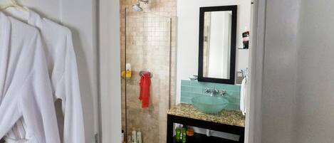A bathroom with a glass shower enclosure, a white towel rack, a sink with a green countertop, and a mirror above the sink.