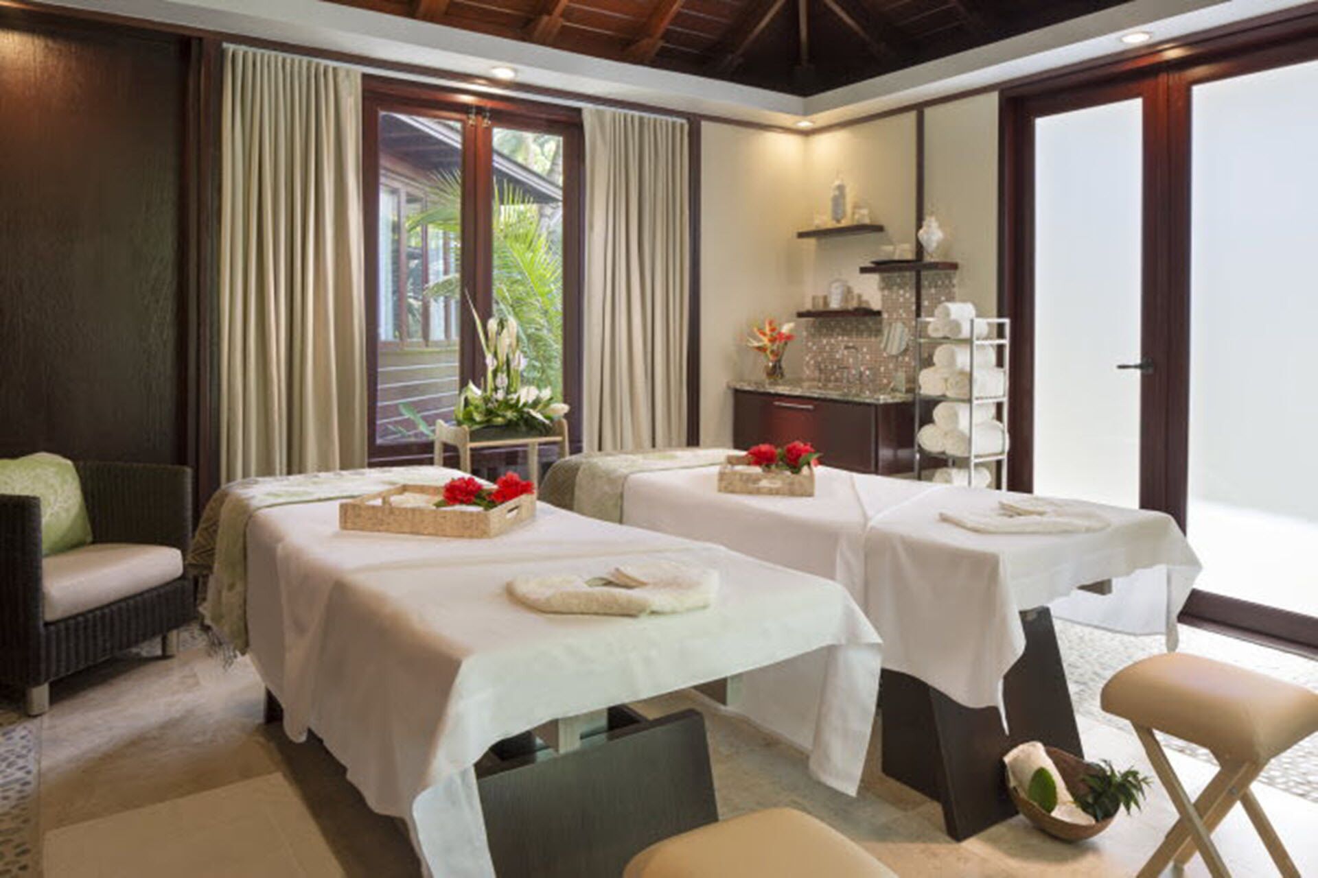 Un cuarto de spa con dos camillas de masaje, un rincón de descanso y vistas al exterior.