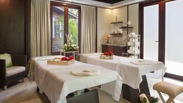 Un cuarto de spa con dos camillas de masaje, un rincón de descanso y vistas al exterior.