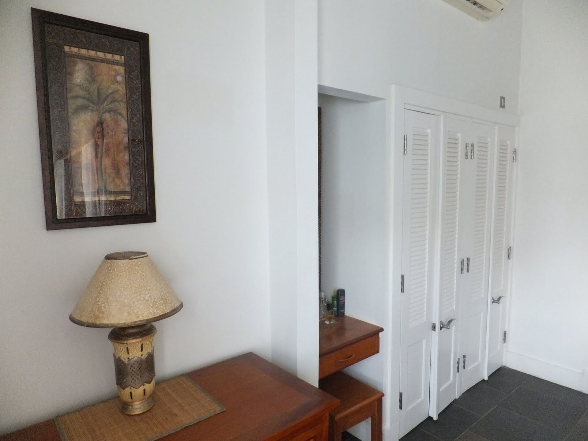 A hallway with a wooden table and a lamp, a framed picture on the wall, and a set of white doors.