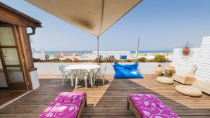 A wooden deck with a table and chairs, a blue bean bag, and two cushioned benches. - Beautiful large 3 bedroom apartment, terrace sea views, Wifi. (Tarifa)