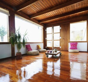 Une pièce spacieuse dotée d’un plancher en bois, de grandes fenêtres et d’un plafond avec des poutres apparentes.